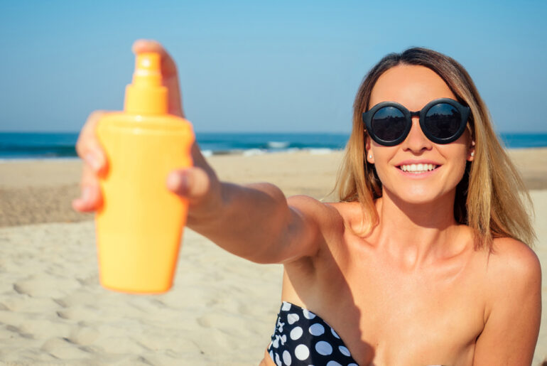beautiful woman sprinkles a sun spray on the beach